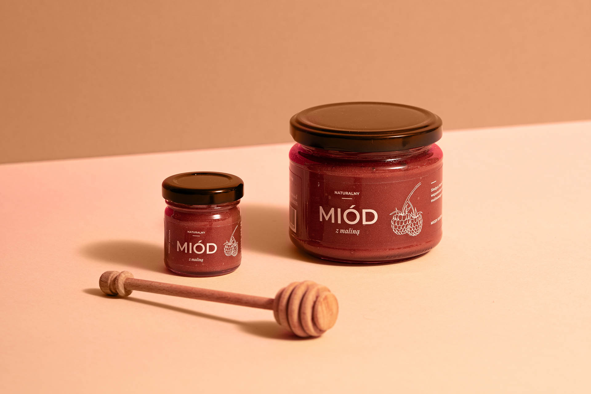 Miód z maliną w postaci większego i mniejszego słoika razem z pałeczką do miodu